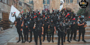 Lions’ Den fighters in their customary black uniforms with red ribbons tied around their rifle barrels.