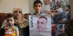 Amal el-Halabi,57,holds her grandson Fares,18 months,while another grandson Amro,7,holds a picture of his father Mohammed el-Halabi,at the family home in Gaza City. The Arabic on the picture reads:“The man of humanity”.