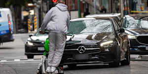 A man rides an e-scooter the wrong way down Little Bourke Street with no helmet in 2024,swerving to miss an oncoming car. 