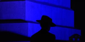 The silhouette of a slouch hat stands out against the blue light projected on the State War Memorial. 