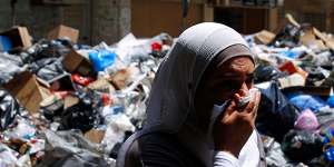 A Lebanese woman covers her nose from the smell as she walks on a street partly blocked by piles of garbage in Beirut on Monday. 