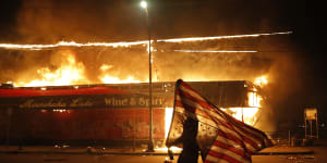 A protester carries the US flag upside down,a sign of distress,next to a burning building in Minneapolis on May 28.