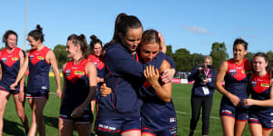 Daisy Pearce,wearing a leg brace,hugs teammate Eliza McNamara after the Demons defeated the Lions.