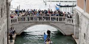 Traditional gondola carrying passengers pass under a bridge full of tourists near Piazza San Marco in Venice.