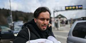 A man carries his one-month-old as he arrives in Poland after crossing the border in Kroscienko on Sunday.