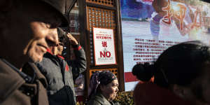 A sign warning against “uncivilised behaviour” is displayed as spectators watch a street performance in the main bazaar in Urumqi,Xinjiang. 