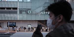 Pedestrians wearing protective masks wait for traffic lights to change near a bus terminal in the Shinjuku district of Tokyo yesterday.