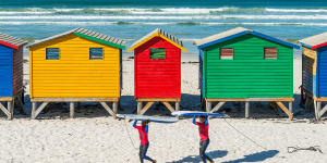 Smiling surfers walking by the beach cabins and huts of Muizenberg,a famous surfing spot near Cape Town.