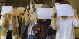 Students in Hong Kong chant “oppose dictatorship” while others hold up blank paper during a vigil for the Urumqi fire victims on Monday. 