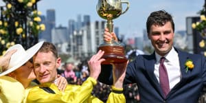 Mark Zahra gets a kiss from wife Elyse after winning the Melbourne Cup as he lifts the trophy with trainer Sam Freedman.