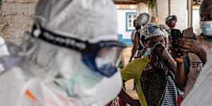 Health workers wearing protective suits prepare for Ebola response operations as residents gather outside a hospital in Mongbwalu,Democratic Republic of the Congo.
