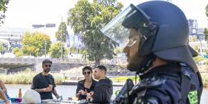 A police officer watches protesters along the Yarra River while Melburnians enjoy a barbecue.