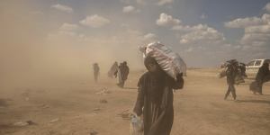 A woman carries supplies from a reception area for people evacuated from the last shred of territory held by Islamic State militants,outside Baghouz,Syria.