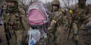 Ukrainian servicemen carry a baby stroller after crossing the Irpin River on an improvised path under a bridge that was destroyed by a Russian airstrike,while assisting people fleeing the town of Irpin,Ukraine,on Saturday.