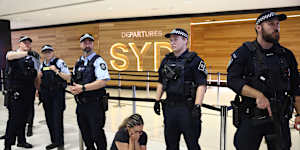 A supporter of the Iranian women’s soccer team is crouched in distress at the knees of police officers in Sydney International Airport.