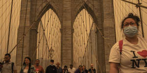 People cross the Brooklyn Bridge amid a dense haze from wildfire smoke in New York.