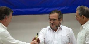 Colombian President Juan Manuel Santos,left,hands the bullet pen to FARC Commander Timochenko,centre,as Cuban President Raul Castro watches.