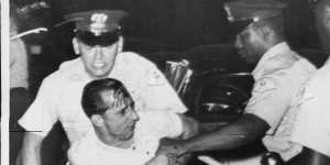 Despite a bloodied head,a white demonstrator grapples with police after fights broke out between black and white people when three black families moved into a predominantly white Chicago suburb in 1963. 