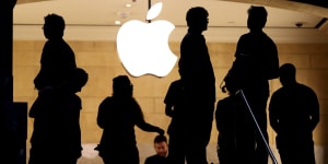 Customers stand beneath an Apple logo at the Apple store in New York.