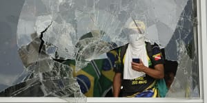 Protesters,supporters of Brazil’s former president Jair Bolsonaro,look out from a shattered window after they storm the Planalto Palace in Brasilia.