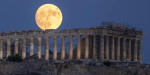 The moon rises in the sky behind the Parthenon at the ancient Acropolis hill,in Athens.