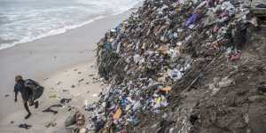 A trash picker walks by piles of textile waste on the shoreline at Chorkor beach in Accra,Ghana. 