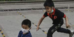 A young Chinese boy pushes a friend who wears a protective masks as he rides on his skateboard while they play at a small park in Beijing.