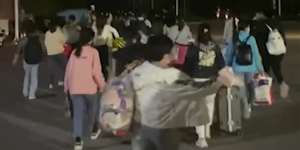 In this photo taken from video footage,people with suitcases and bags are seen leaving from a Foxconn compound in Zhengzhou.