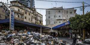 A restaurant worker takes bags of trash to add to a giant pile of garbage left uncollected for a week outside a bar named Floyd the Dog in Beirut.