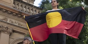 A protester holds an Aboriginal flag at a rally to mark 30 years since the royal commission. into deaths in custody.