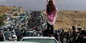 A girl with uncovered head stands atop a car during protests in Iran.