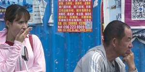 People wait in front of advertisements in Chinese pasted on a fence outside a construction site in Sihanoukville,Cambodia.