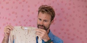Tom Bull holds an infant’s outfit that was purchased in anticipation of welcoming his first child.