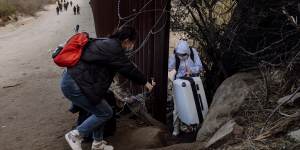 Migrants cross through a gap in the US-Mexico border fence in Jacumba Hot Springs,California.