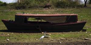 A bird walks past a boat sitting on the side of the almost dried up Payagua stream,a tributary of the Paraguay River.