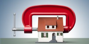 Clamp squeezing model house. Money cover. Locking in interest rates on your mortgage story. Property. Housing. Finance. Image by iStock Photo.