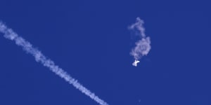 The remnants of the large balloon drift above the Atlantic Ocean,with a US fighter jet and its contrail seen below it.