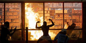 A man poses for photos in front of a fire at an AutoZone store,while protesters hold a rally for George Floyd in Minneapolis on Wednesday.