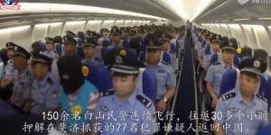 A hooded person,suspected of cyber scams,sits between Chinese police officers on a charter plane from Fiji to China in 2017.