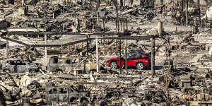 A car drives past homes and vehicles destroyed by the Palisades fire at the Pacific Palisades Bowl Mobile Estates.