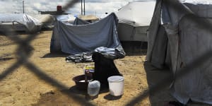 A woman washes clothes in front of her tent at the fence line of the Foreign section of al-Hawl camp in Syria.