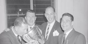 Melbourne coach Norm Smith drinks a victory toast from the 1960 VFL premiership cup,watched by John Beckwith,John Lord and Barassi after their win over Collingwood.