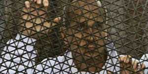 Al Jazeera journalist Peter Greste stands inside the defendants'cage in a courtroom during a trial on terror charges,along with several other defendants,in Cairo Egypt.