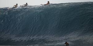 Surfers paddle over the top of a wave in Teahupo’o,Tahiti.
