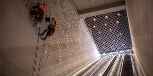 Workers abseil a wall to assemble a giant artwork of 1000 Indigenous footprints.