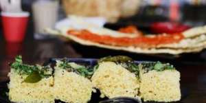 Khaman dhokla,in the foreground,is a steamed cake sprinkled with mustard seeds and curry leaves.