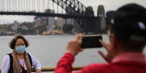 People wearing face masks as a preventative measure against coronavirus COVID-19 take photos in front of the Sydney Harbour Bridge in Sydney.