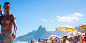 A beach vendor selling caipirinhas calls out to customers on Ipanema Beach with Two Brothers mountain backdrop.