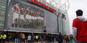 Fans walk past a poster of the Busby Babes on the front of Manchester United’s Old Trafford Stadium.