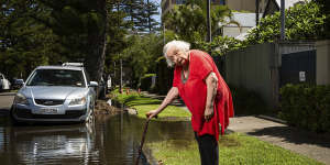 Jane Hester stands outside a huge flow of water on Malvern Avenue,Manly. It has been getting worse for nearly a fortnight.